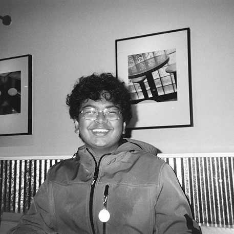 Manitej smiling in front of a wall of framed photos